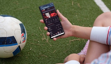 Mulher segurando um celular em um campo de futebol com mockup da Onabet